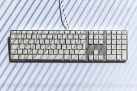 Minimalist white computer keyboard on a clean desk with striped light shado.. Stock Photos