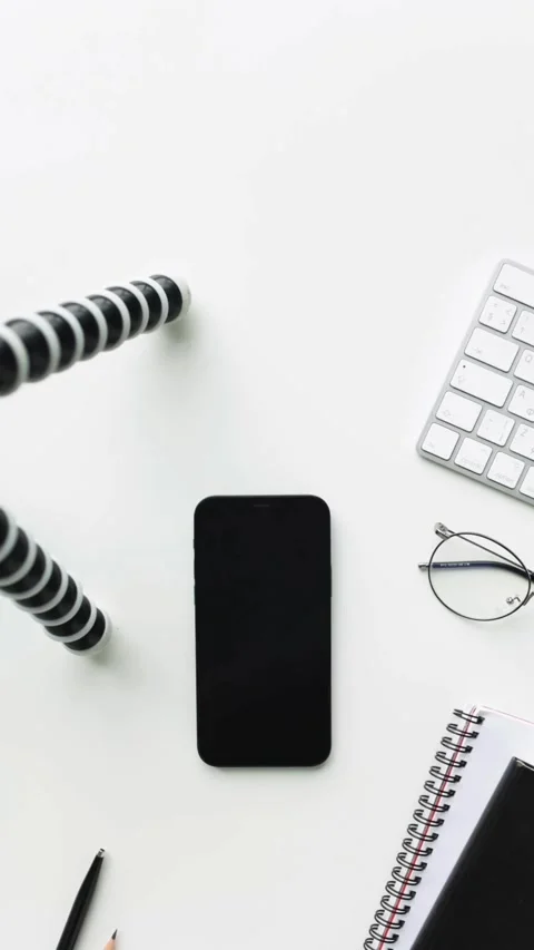 Minimalist white desk features smartphone keyboard glasses and notebook Video stock 331769849