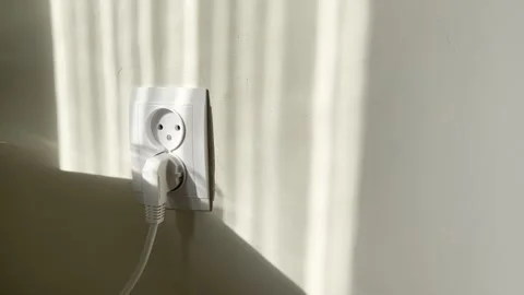 Minimalist white wall electrical outlet connects sleek power cable through soft Vídeos de archivo 334655881
