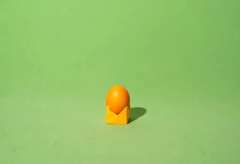 Minimalistic composition of orange painted easter egg on paper stand in the c Stock Photos