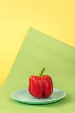 Minimalistic composition of red bell pepper, blue plate yellow green background Photos