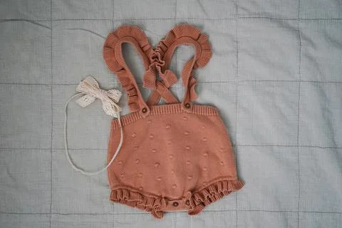 Minimalistic flat lay of a stylish knitted baby romper with ruffles and a vin Stock Photos