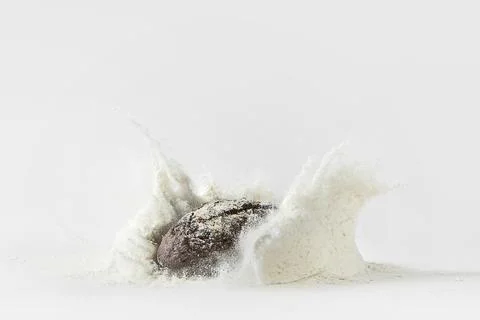 Minimalistic picture - rye bread falling into flour on a white background Stock Photos