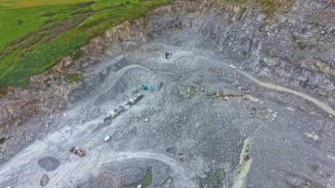 Mining activity takes place in a large open quarry surrounded by green hills and Stock Footage 340178411