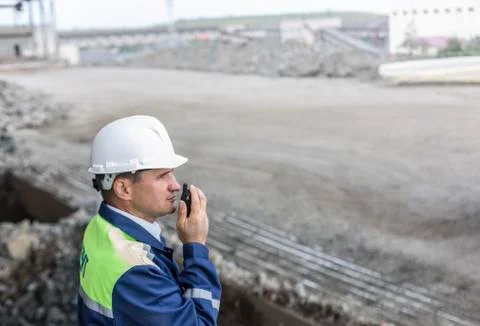 Mining engineer in yellow-blue uniform white helmet supervises unloading dumpers Foto stock