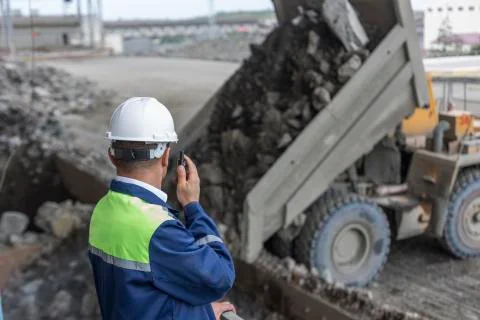 Mining engineer in yellow-blue uniform white helmet supervises unloading dumpers Stock Photos