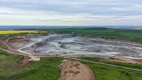 Mining operation takes place in a large open pit surrounded by green fields and Stock Footage 342470246