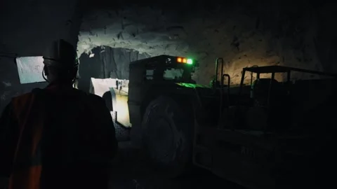 Mining ore underground in the dark. Excavator collects ore. A worker in a helmet Stock Footage 240715382