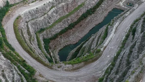 Mining road looping tightly around flooded trench carved into terraced rock. Stock Footage 323594016