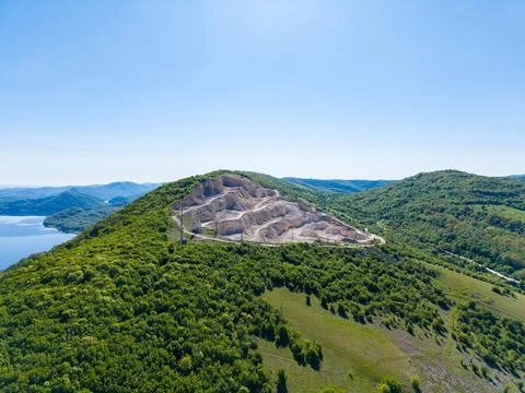 A mining site is visible on a hillside surrounded by green trees and a lake i Stock Photos