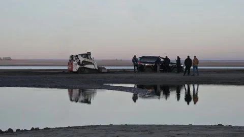 A minitractor is trying to pull out a stuck car in the river. Stock Footage 303139479