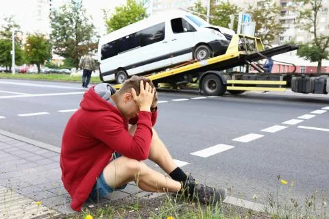 Minivan driver sits on side of road and holds his head during evacuation of his Stock Photos