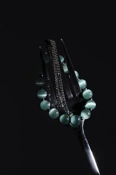 Mint Green Beaded Bracelet Draped Over Metal Fork on Black Background Stock Photos