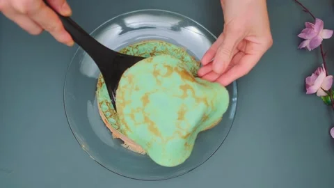 Mint green pancake being plated indoors on a gray surface Видео 342880506