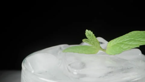 Mint leaves are lying on ice cubes in a glass of soda, a close-up panorama on a  Stock Footage 231749129