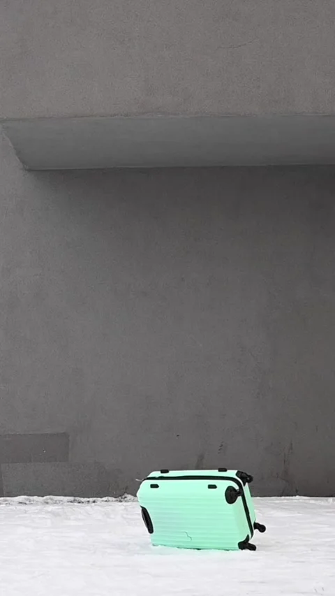 A mint plastic suitcase on wheels falls from a height onto the snow against a Stock Footage 274358858