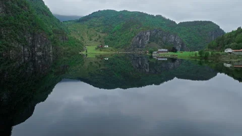 Mirror-like lake surrounded by mountains and Norwegian houses in rural Norway. Stock Footage 328132272