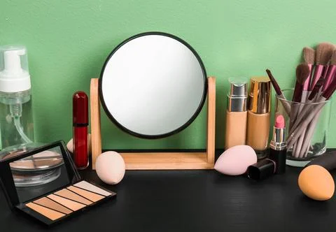 Mirror, makeup brushes and different cosmetics on table near green wall in ro Stock Photos