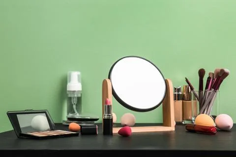 Mirror, makeup brushes and different cosmetics on table near green wall in ro Stock Photos