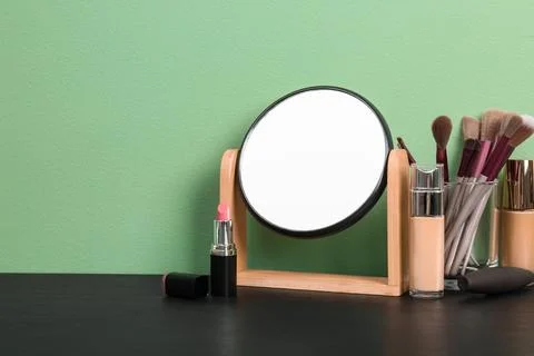 Mirror, makeup brushes and different cosmetics on table near green wall in ro Stock Photos