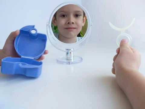 Mirror refclection of small boy,his hands holding orthodontic device,cap,and box Stock Photos