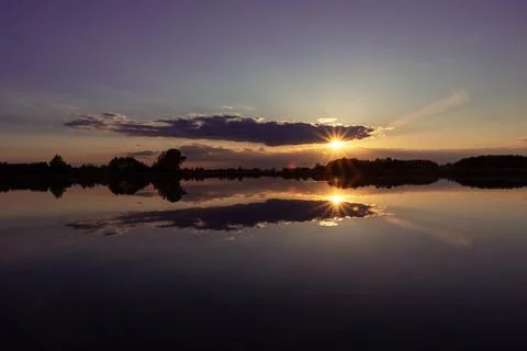 Mirror reflection of clouds and sunset in the water of a calm lake Stock Photos