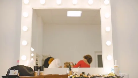 Mirror reflection of the makeup artist and hairdresser preparing blonde model at Stock Footage 74428973