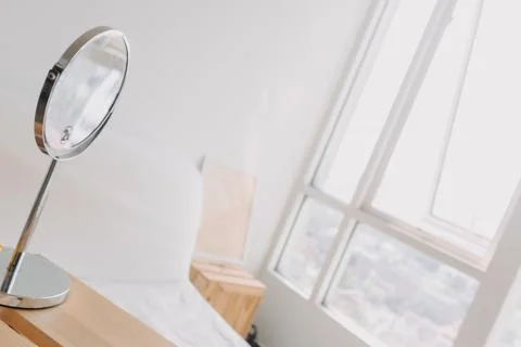 A mirror is sitting on a table next to a window in a bedroom Stock-Fotos
