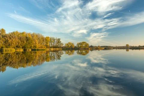 Mirroring clouds in a quiet lake, trees on the horizon Stock Photos