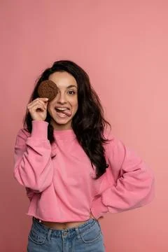 Mischievous dark-haired lady posing with an oat biscuit on the pink background Stock Photos