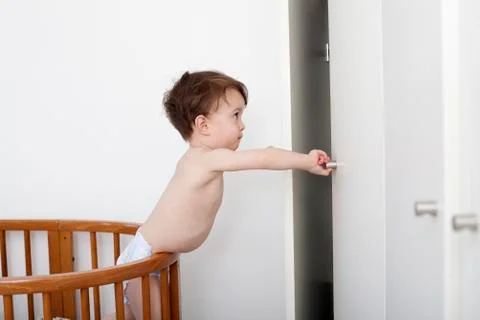 A mischievous toddler reaching out to open a closet door from his crib Stock Photos