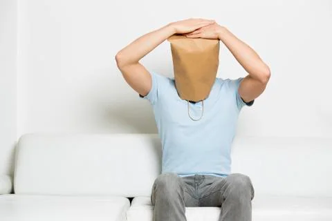 Miserable anonymous man with head covered sitting on sofa. Stock Photos