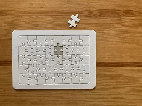The missing piece of an all-white jigsaw puzzle put on the wooden table Stock Photos