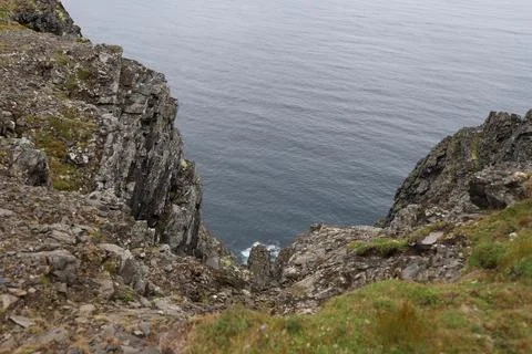Mist-covered arctic cliffs meet the calm ocean on a hazy summer day at Nordka Stock Photos