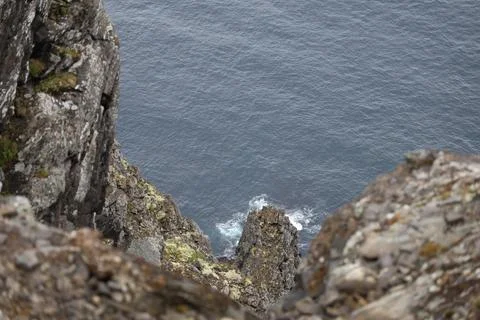 Mist-covered arctic cliffs meet the calm ocean on a hazy summer day at Nordka Stock Photos