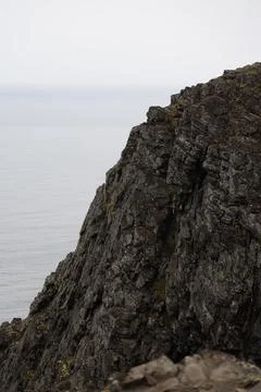 Mist-covered arctic cliffs meet the calm ocean on a hazy summer day at Nordka Stock Photos