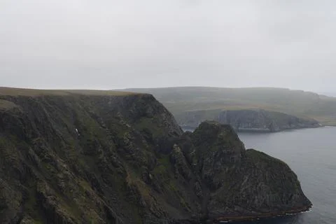 Mist-covered arctic cliffs meet the calm ocean on a hazy summer day at Nordka Stock Photos