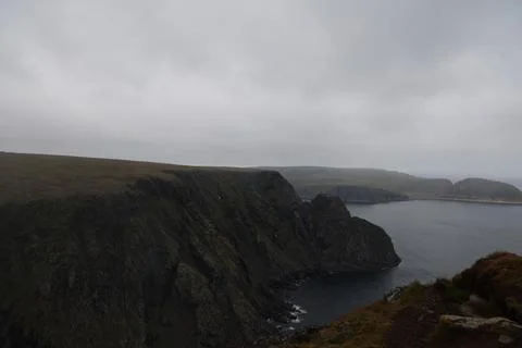 Mist-covered arctic cliffs meet the calm ocean on a hazy summer day at Nordka Stock Photos
