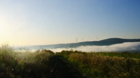 Mist flow covers mountain bottom windmills work under blue sky Video stock 323881080