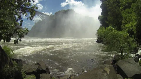 Mist with large cliff behind framed by tropical trees and flowing Zambezi River Видео 22871385