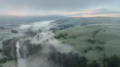Misted patchwork field hillside with river shrouded by mist and dawn glow 動画素材 276052966