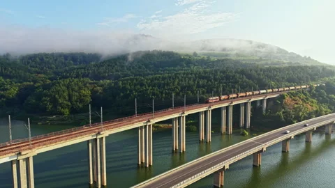 Misty elevated bridge carrying freight train and vehicle traffic over river Stock Footage 341390695