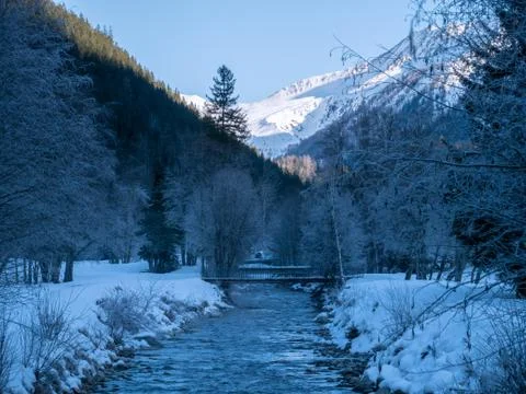 A misty mountain stream flows through a snowy landscape. Stock Photos