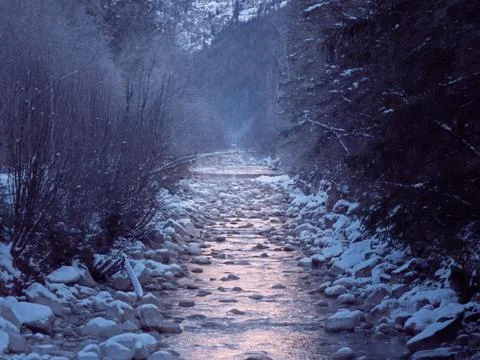 A misty mountain stream flows through a snowy landscape Stock Photos