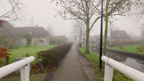 Misty Path With Lampposts And Trees, Footbridge Spans Foggy Canal With Distant Stock Footage 325451724