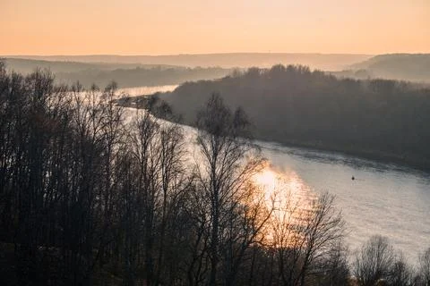 A misty river bend at sunset with bare trees on hazy banks and the reflection Stock Photos
