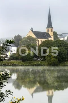 Misty river valley with church in treed area reflecting in the river Stock Photos