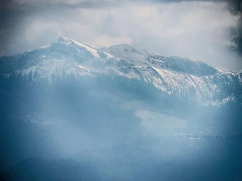 A misty, snow-capped mountain range under a cloudy sky. Stock-Fotos