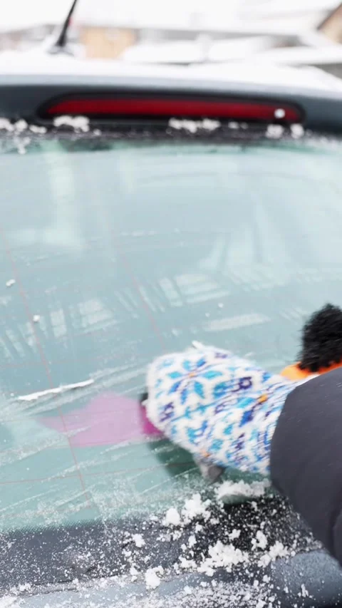Mittened hand brushes snow and scrapes frost from a rear windshield, clearing Stock Footage 327829918