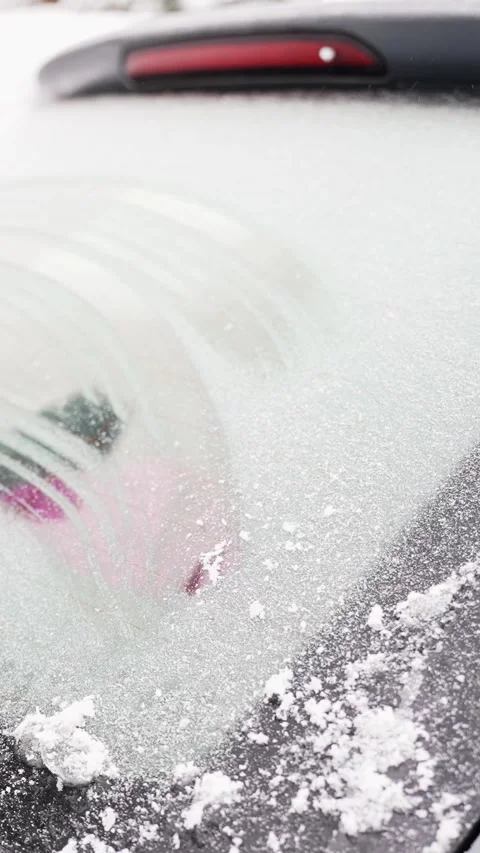 Mittened hands use an ice scraper and snow brush to break thick ice on a car Stock-Footage 327689863